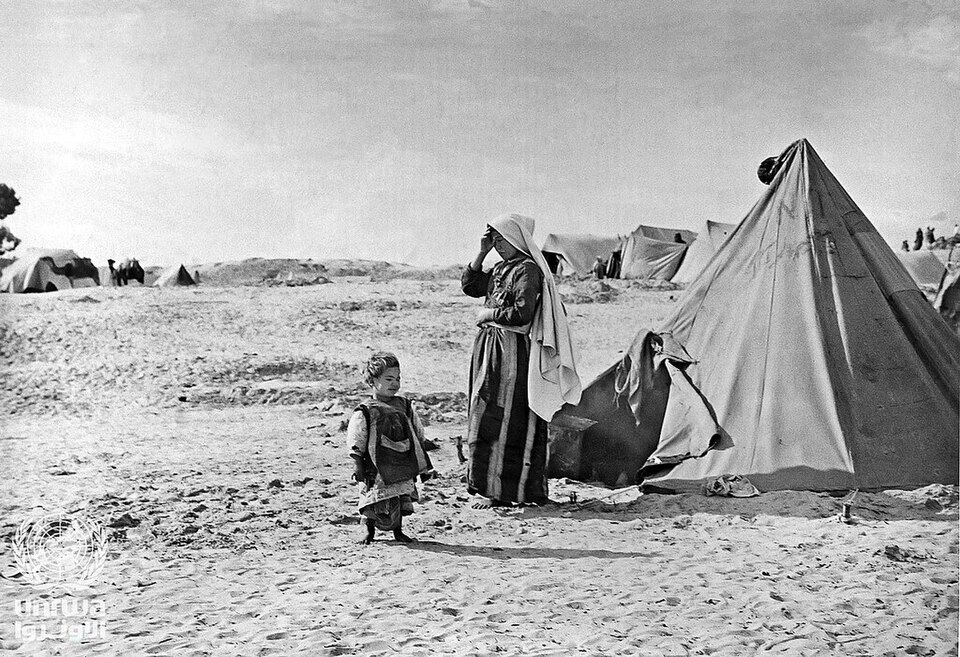 Mother and child standing next to their tent in a refugee camp